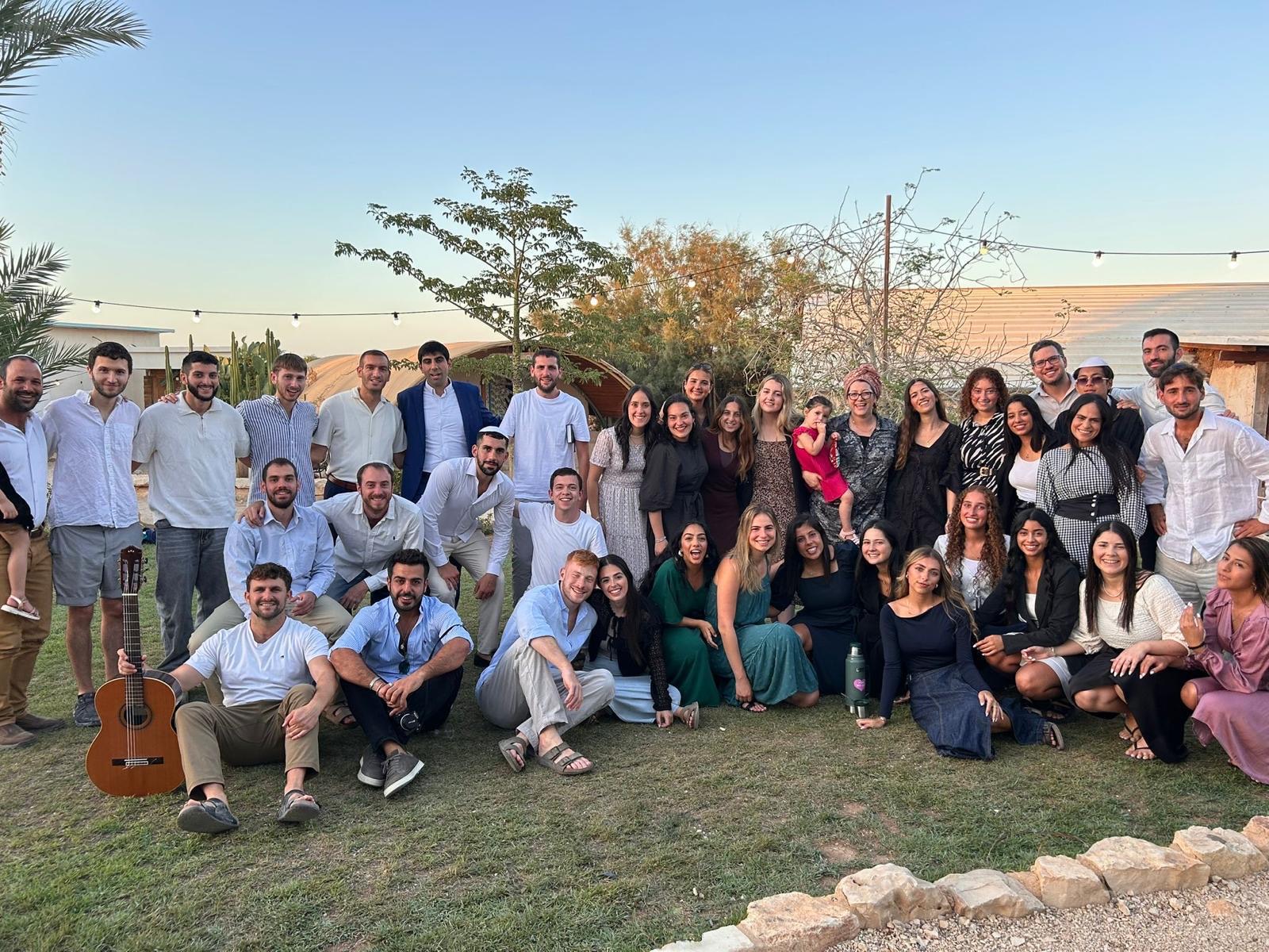 Grupo de la comunidad de La Casa TLV reunido al atardecer en un jardín, con guirnaldas de luces